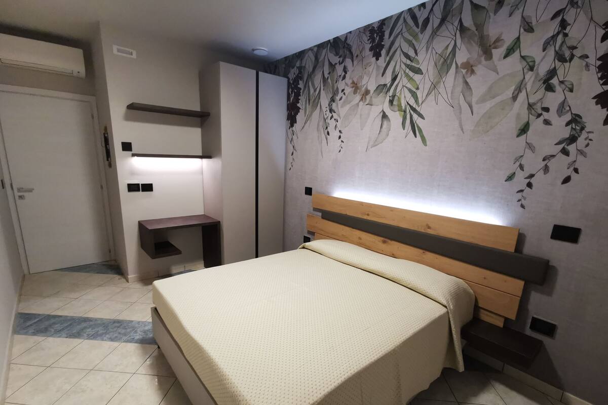 Una camera da letto con un letto, un comodino, una mensola a muro e una parete con un murale floreale.