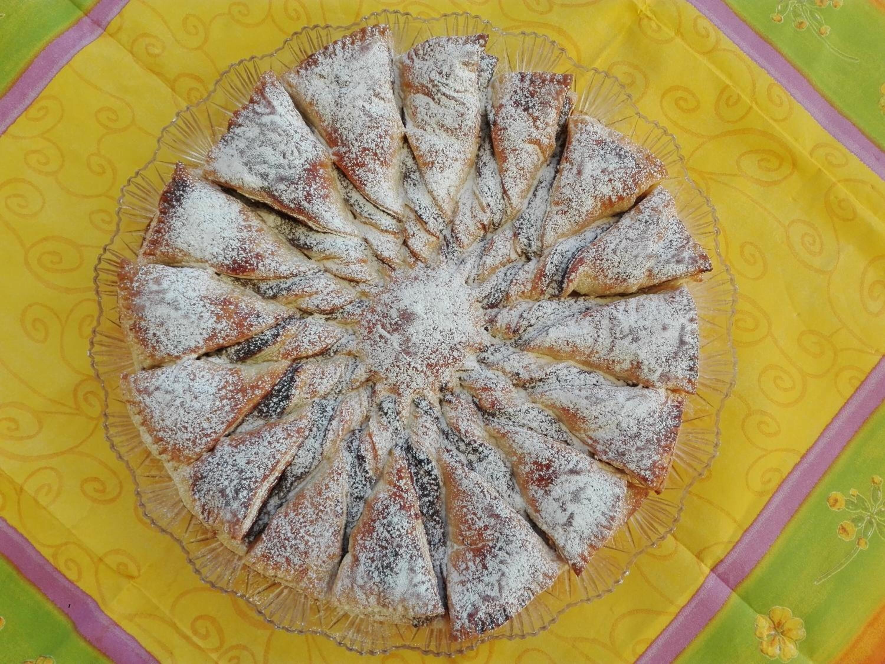 Un pastel redondo con porciones triangulares sobre un mantel amarillo estampado.