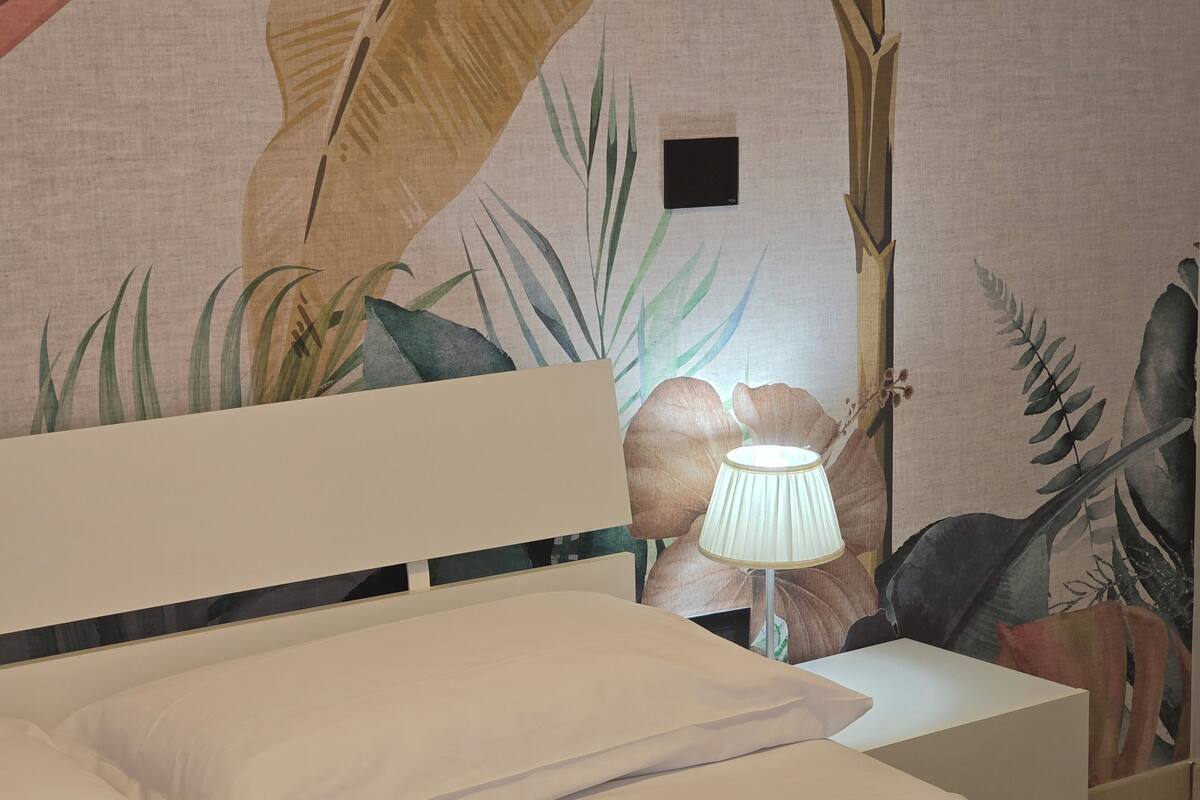 Un letto con biancheria bianca, un comodino bianco e una lampada.