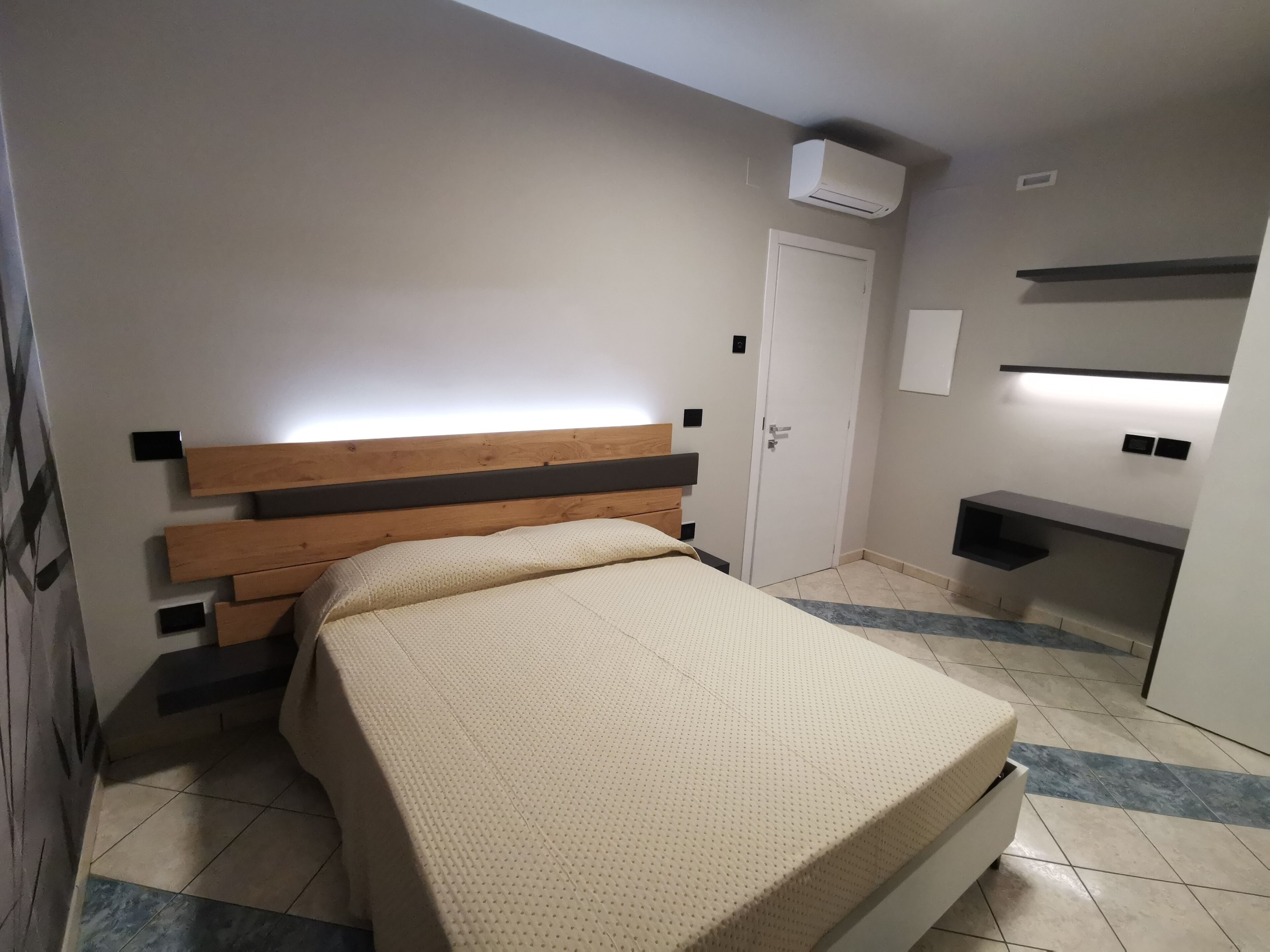 A bedroom with a wooden headboard, a bed with a textured cover, a white door, and a built-in shelf.