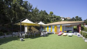 Un patio con mobiliario exterior, una zona de juegos cubierta y un edificio con paredes coloridas.
