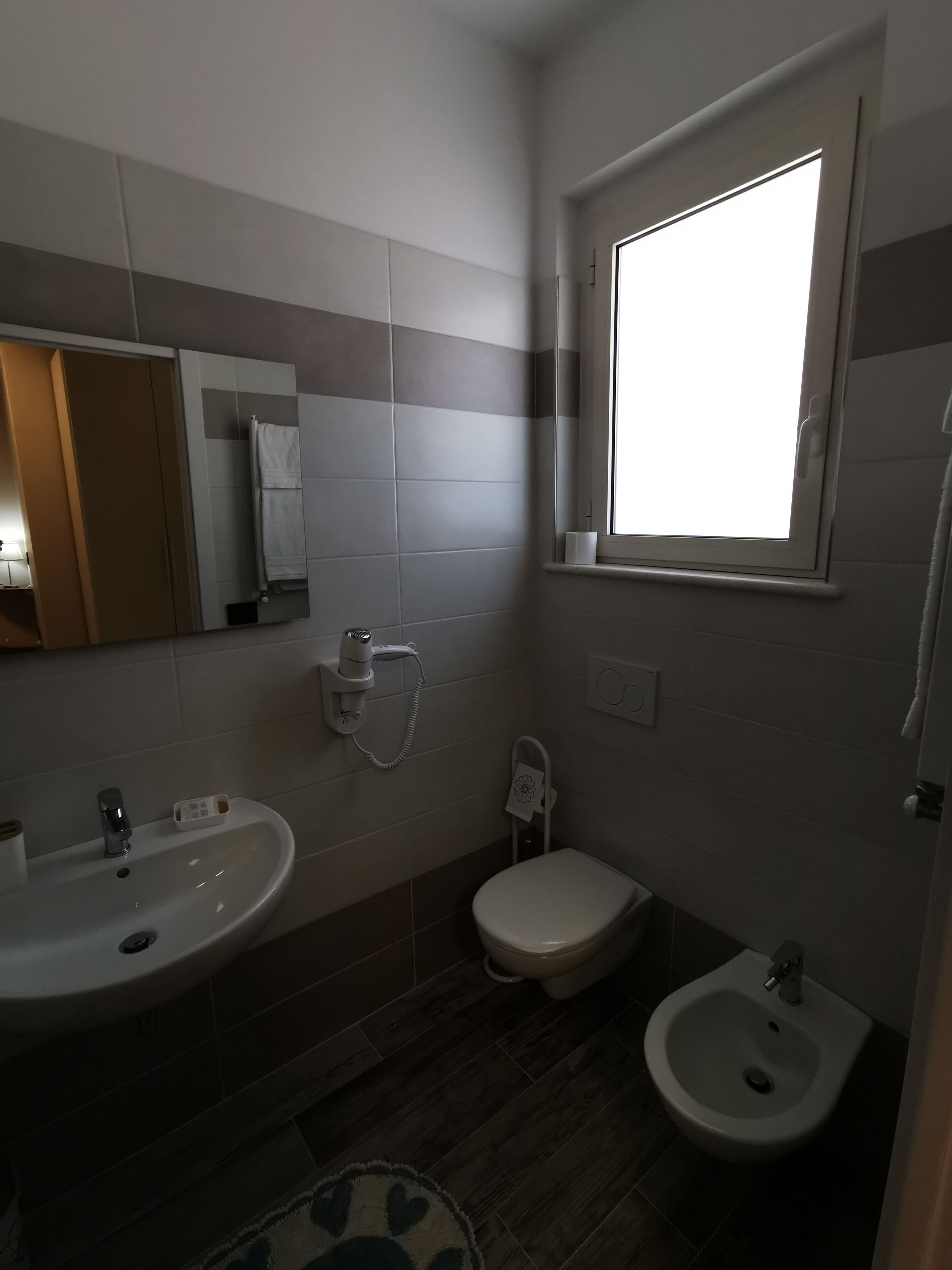 Un baño moderno con lavamanos, inodoro, bidé y ventana que proporciona luz natural.