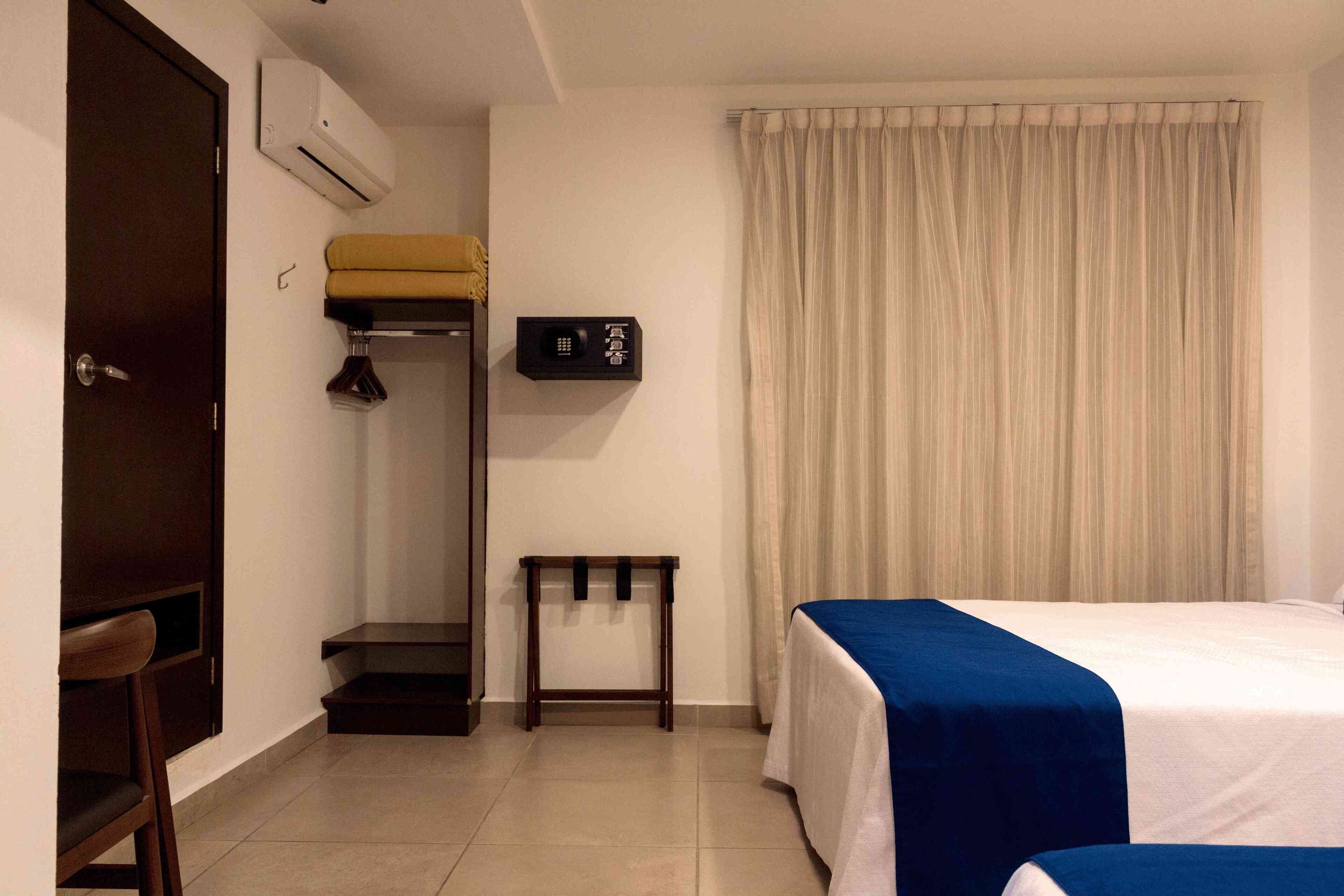 A hotel room with a bed, a desk, a wardrobe, and a window with curtains.