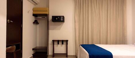 A hotel room with a bed, a desk, a wardrobe, and a window with curtains.