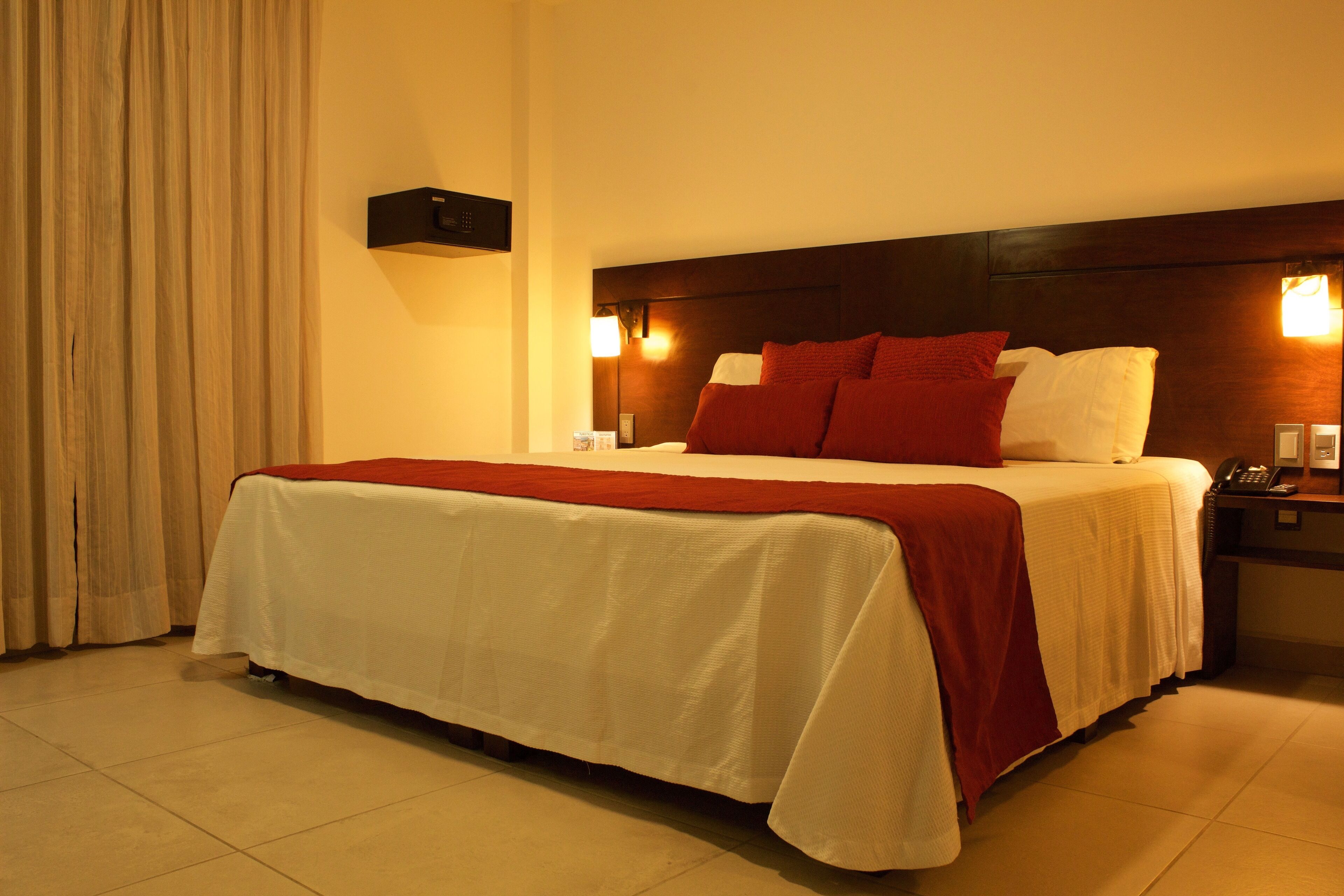 Una habitación de hotel con una cama grande, una mesita de noche, un teléfono y una lámpara fijada a la pared.