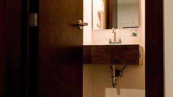 A bathroom with a wooden door, a sink with a mirror, and a light fixture above the mirror.