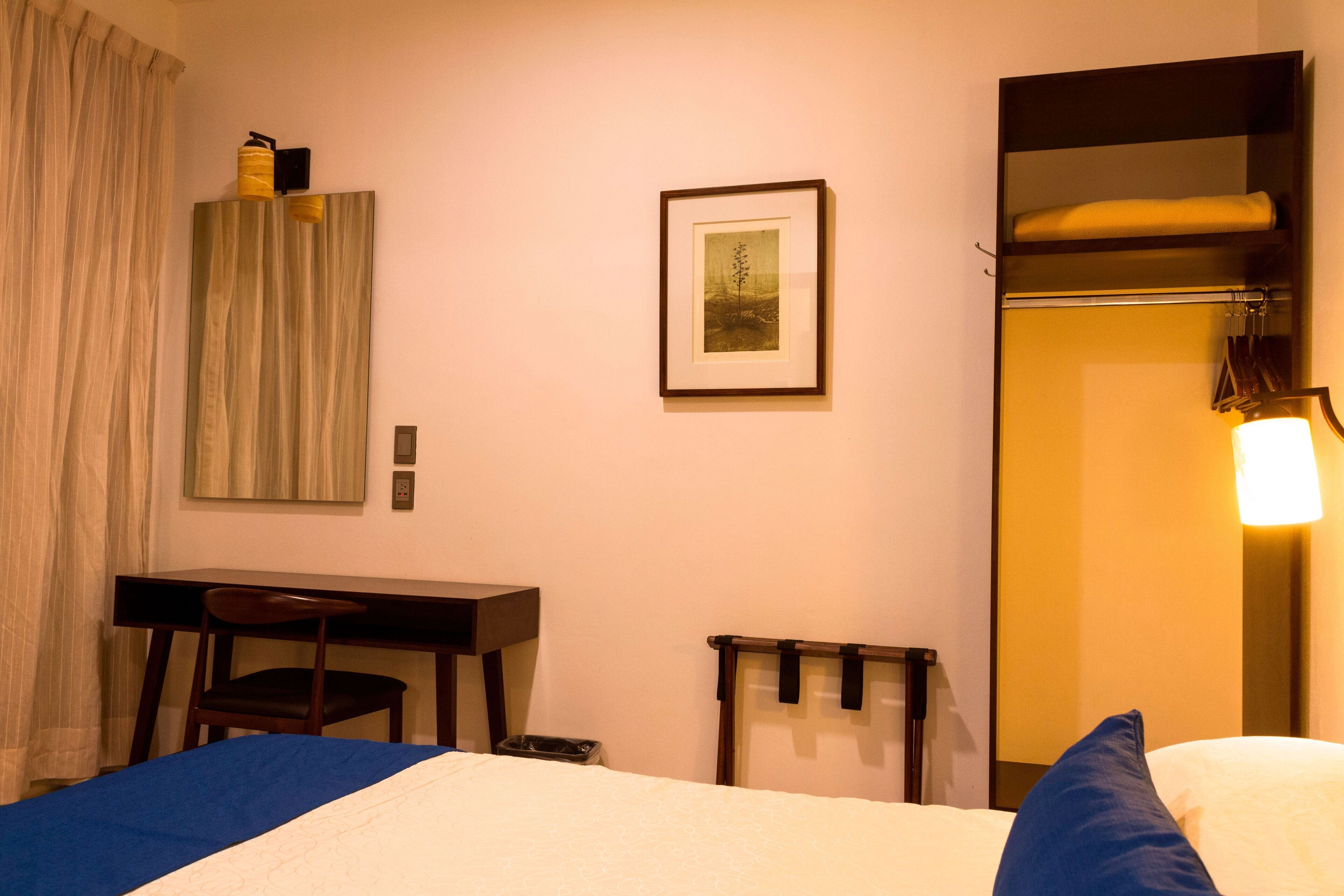 A hotel room with a bed, a desk, a chair, a framed picture on the wall, and a wardrobe.