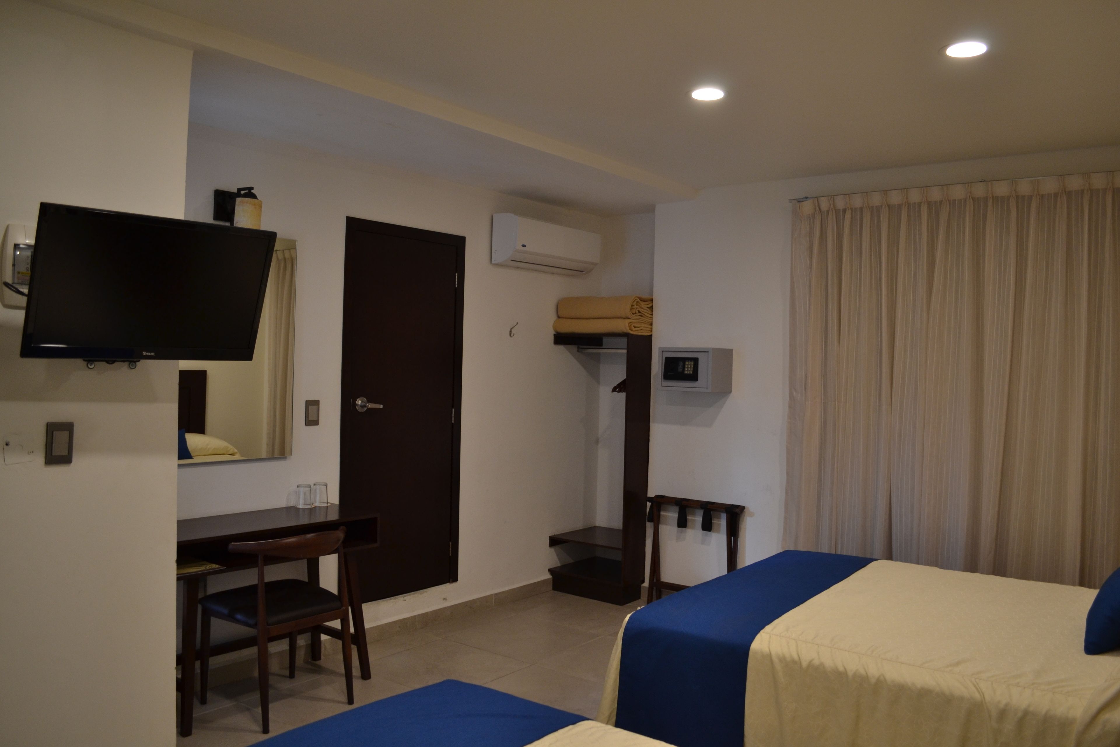 A hotel room with a bed, a desk, a chair, a television, and an air conditioning unit.