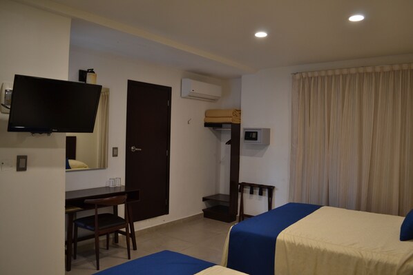 Una habitación de hotel con cama, escritorio, silla, televisor y aire acondicionado.