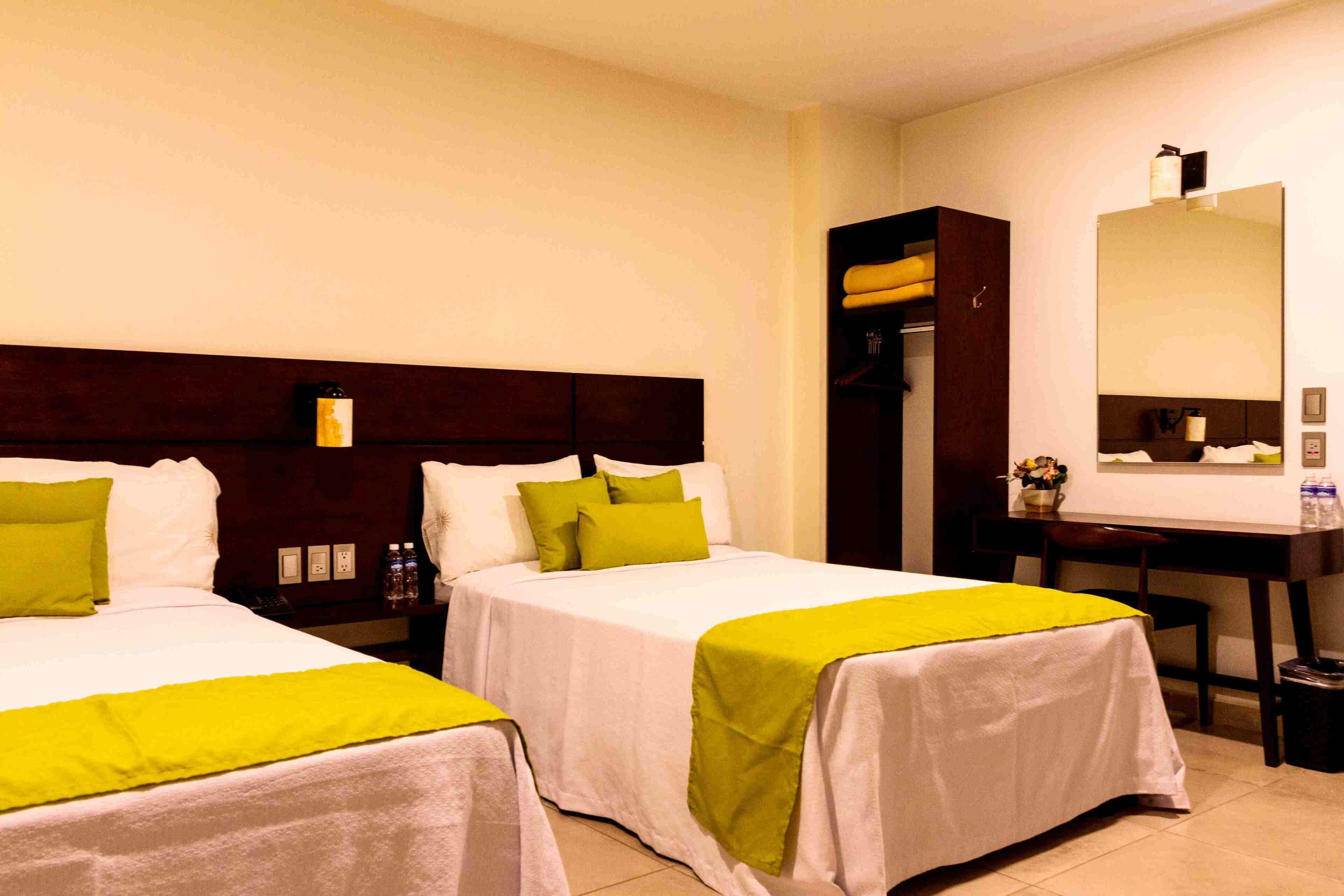 A hotel room with two beds, a desk, a chair, a mirror, and a wardrobe.