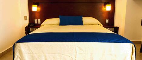 A hotel room with a large bed, two bedside tables, a nightstand, and a wall-mounted telephone.