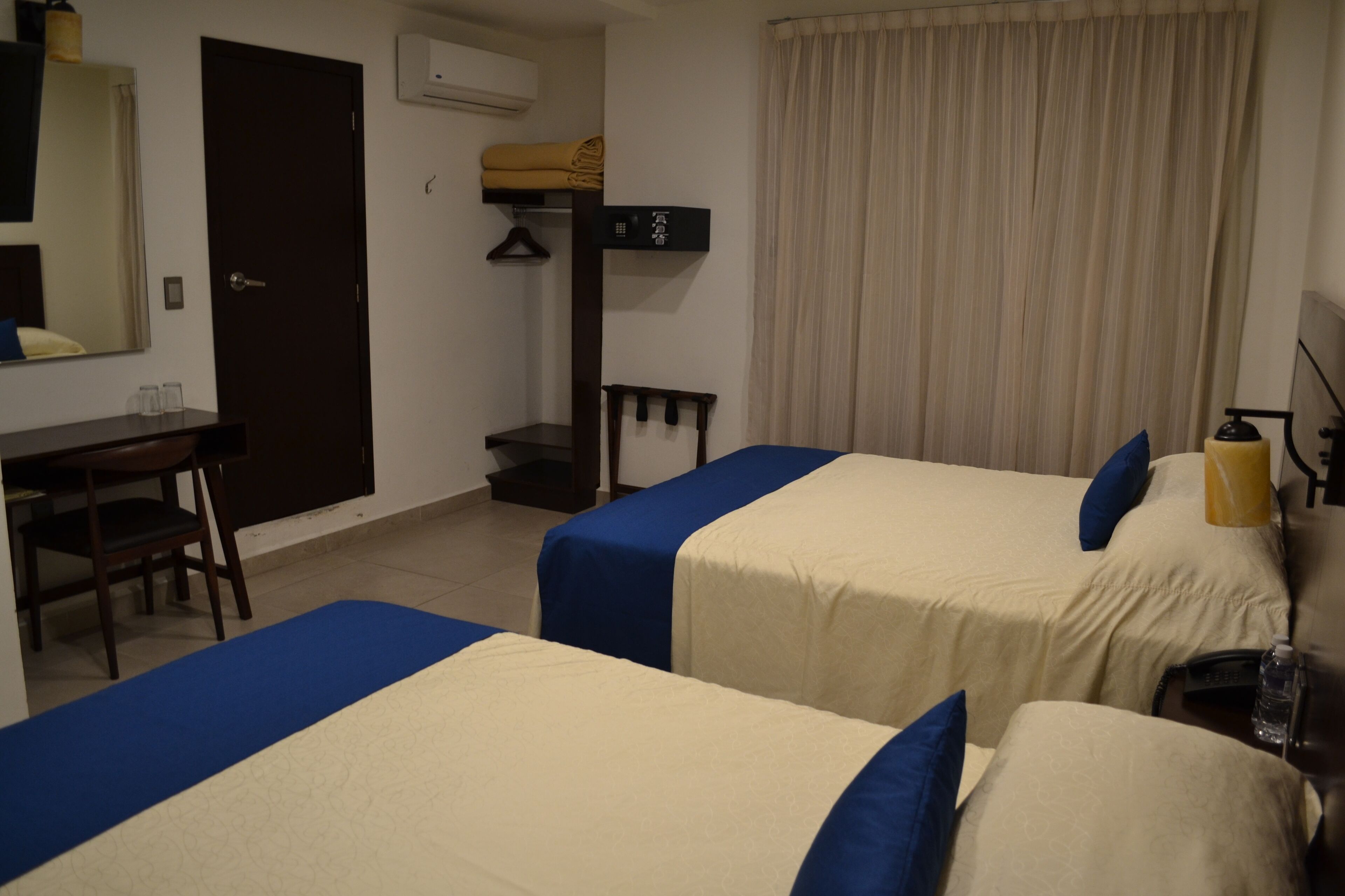Ein Hotelzimmer mit zwei Betten, einem Schreibtisch, einem Stuhl, einem Kleiderschrank und einem Fenster mit Vorhängen.