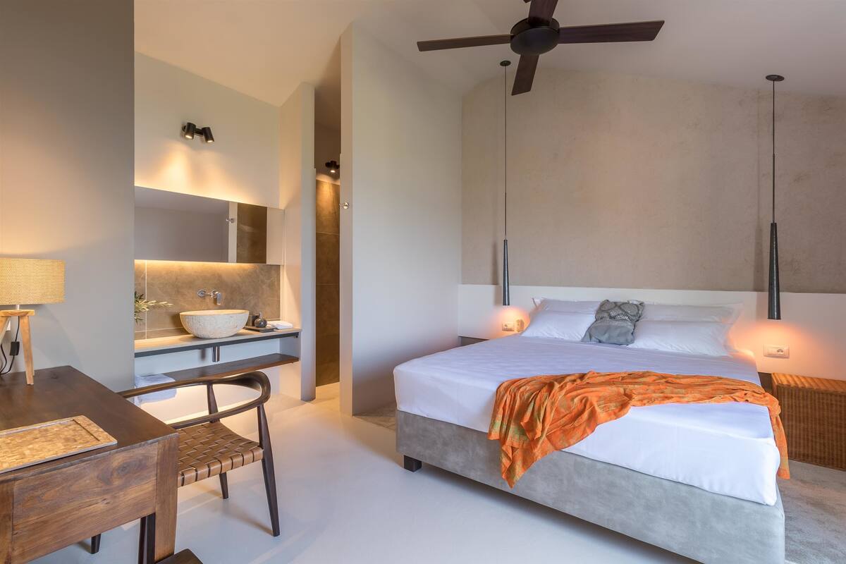 A modern bedroom with a large bed, a desk, and a bathroom with a vanity.