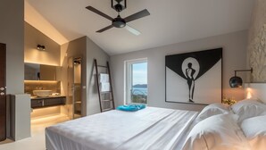 Een moderne slaapkamer met een groot bed, een plafondventilator, een badkamer met een wastafel en uitzicht op de omgeving.