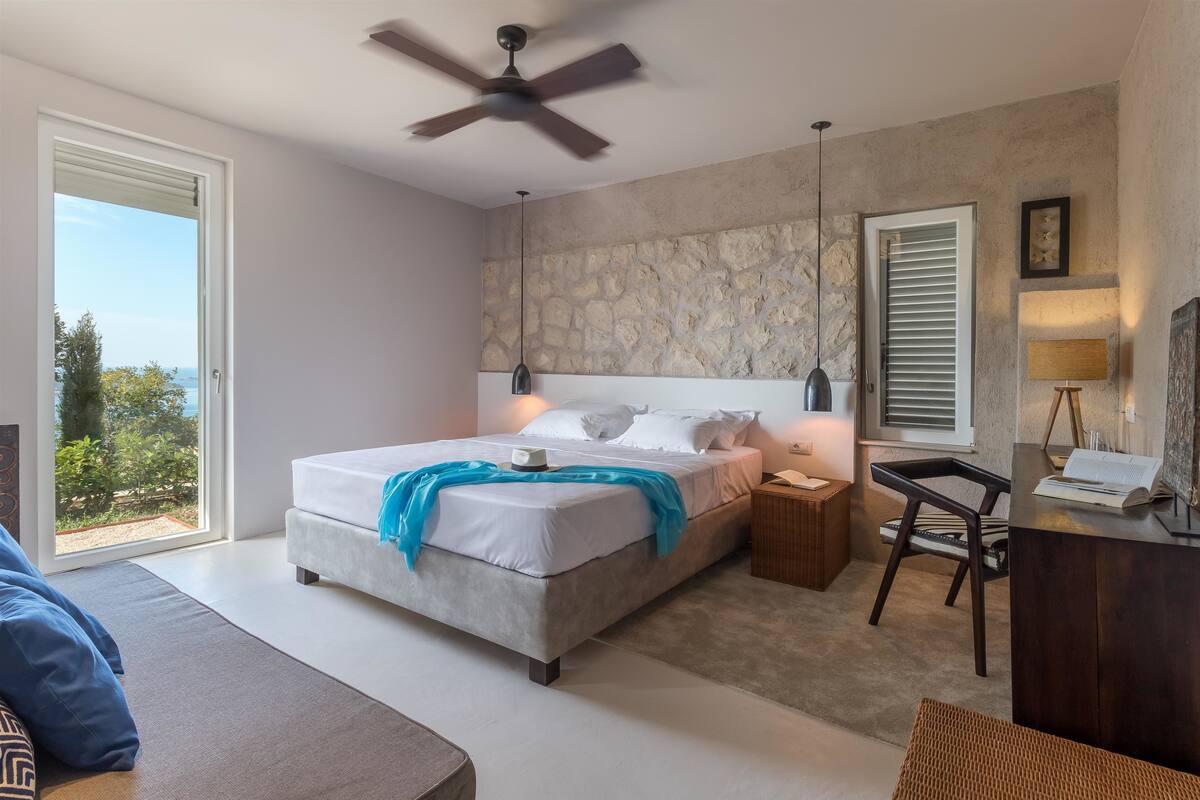 A bedroom with a bed, bedside tables, a desk, and a view of the outdoors.