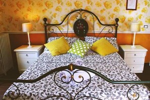 A bed with a patterned bedspread, two pillows, a decorative headboard, and bedside tables with lamps. - Hostel Relaxon247 (Rome)
