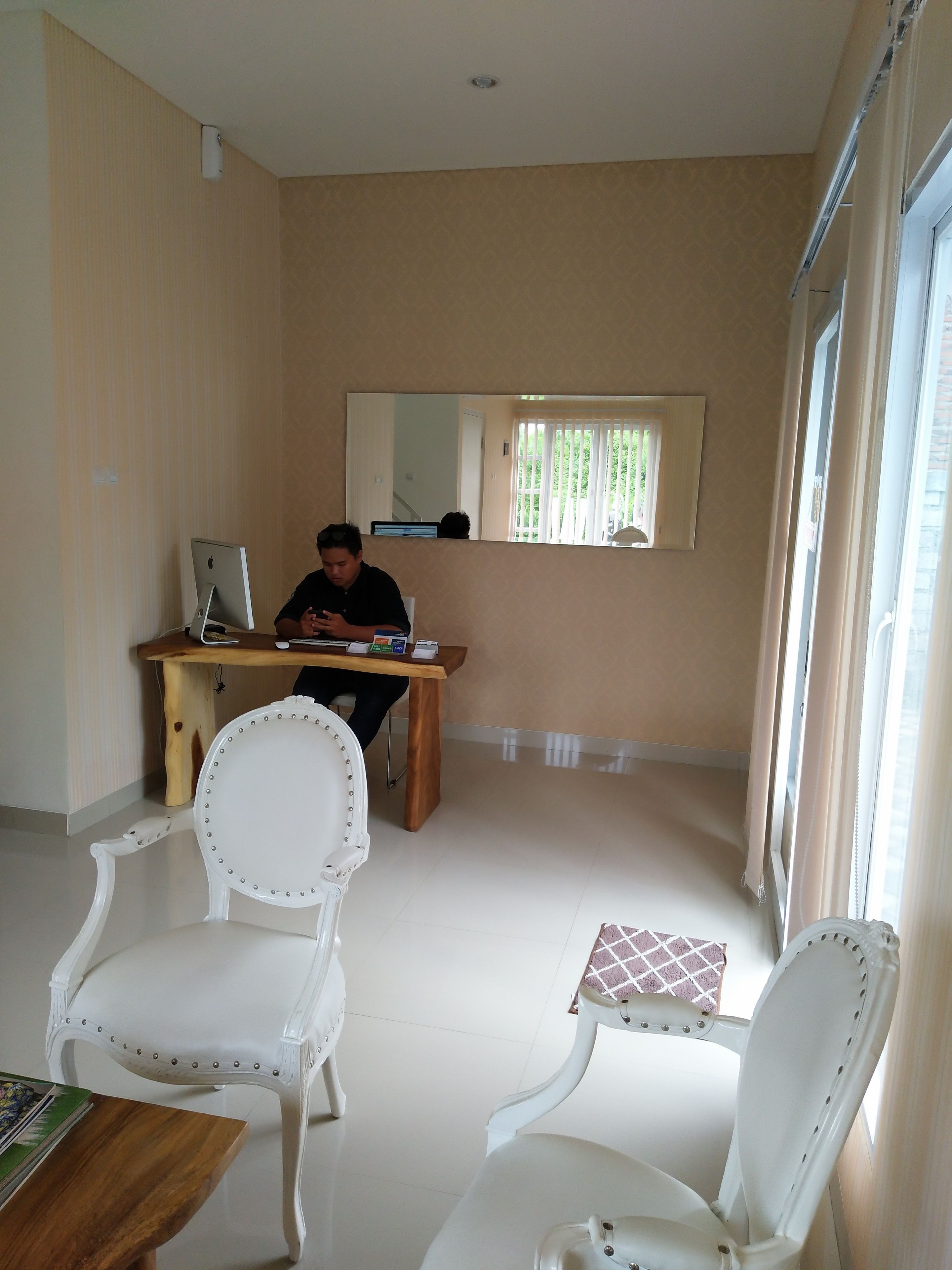 Een kamer met een bureau, twee witte stoelen, een computer en een raam met jaloezieën.