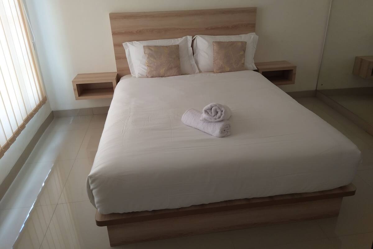 Un lit bien fait, avec une serviette pliée, une tête de lit en bois et deux tables de chevet avec des lampes.