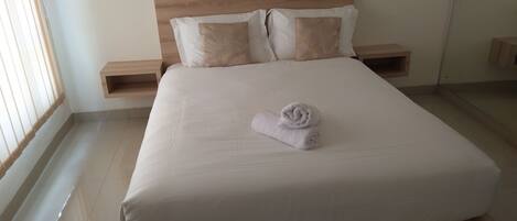 A neatly made bed with a rolled towel, wooden headboard, and two bedside tables with lamps.