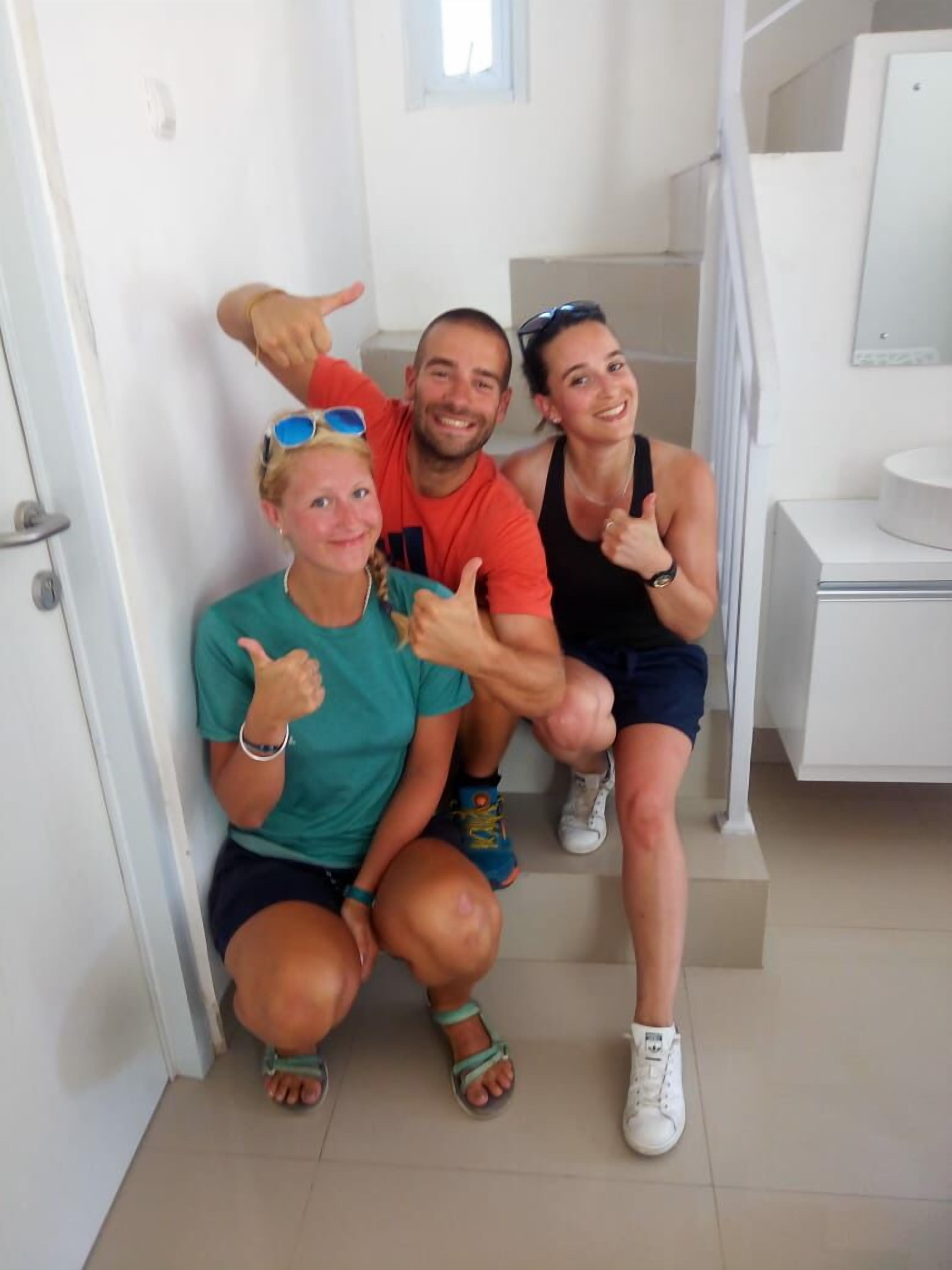 Three people posing in a modern bathroom with a white sink and a mirror.