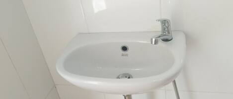 A white bathroom sink with a chrome faucet and a small trash bin beside it.