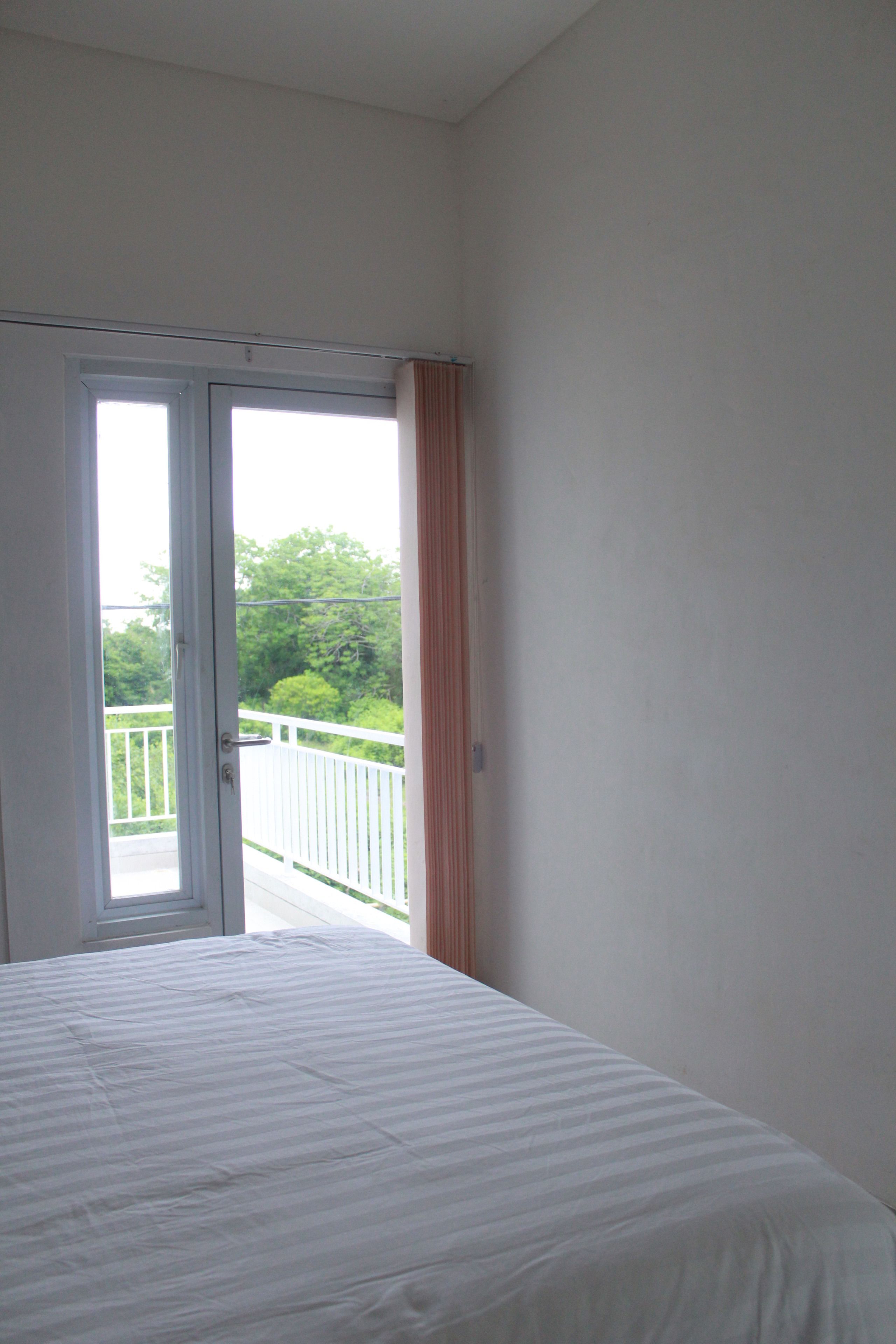 Ein Schlafzimmer mit einem Bett, einer Tür zu einem Balkon und Blick ins Grüne.