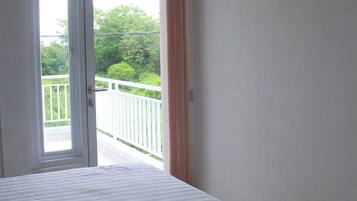 Ein Schlafzimmer mit einem Bett, einer Tür zu einem Balkon und Blick ins Grüne.