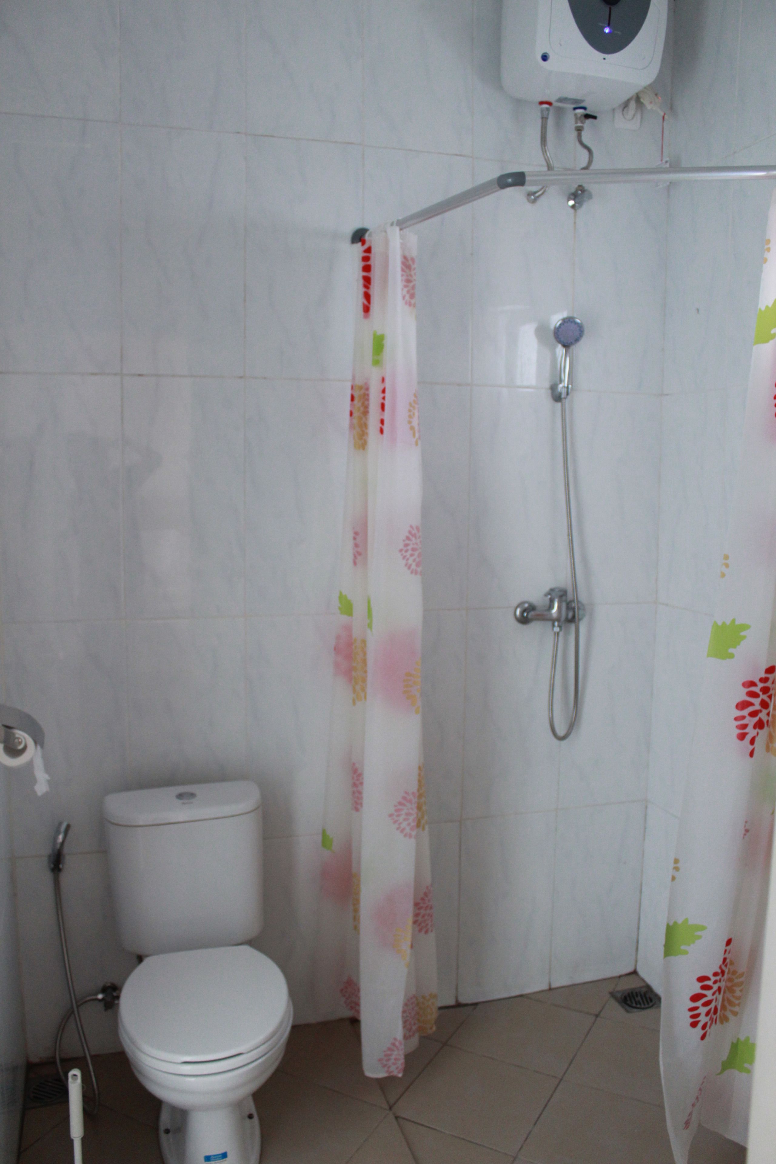 A bathroom with a toilet, shower, and a hand dryer.