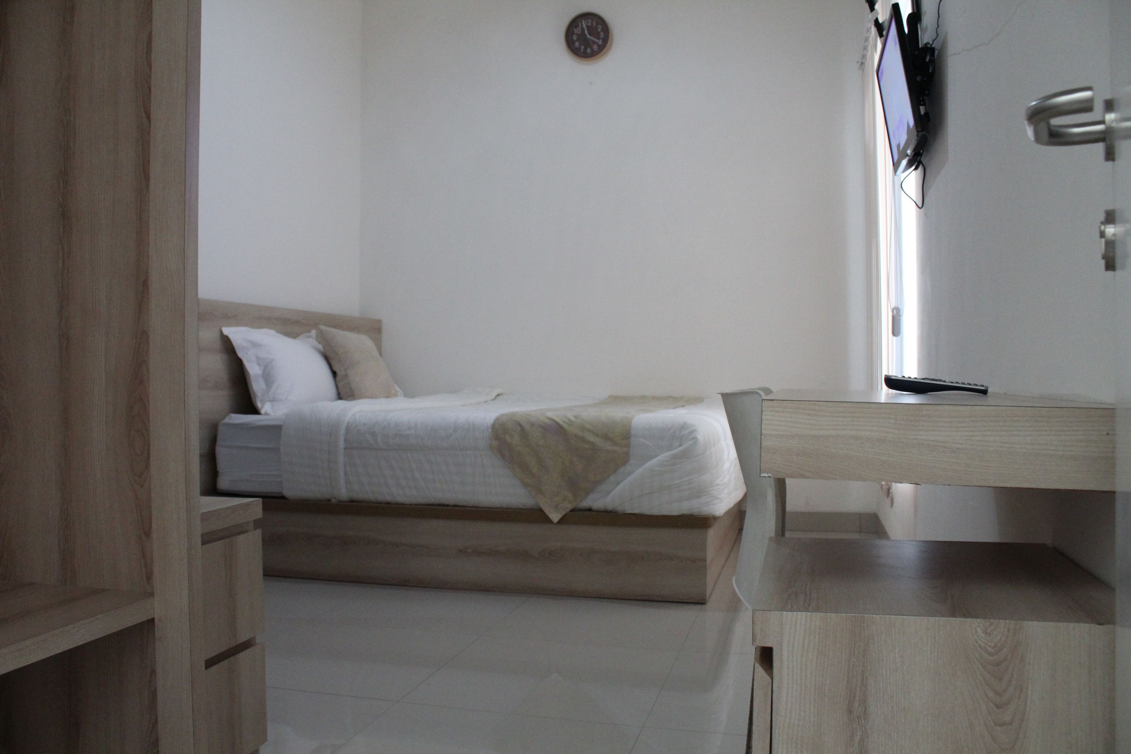 Een slaapkamer met een bed, een nachtkastje, een aan de muur bevestigde televisie en een houten garderobe.