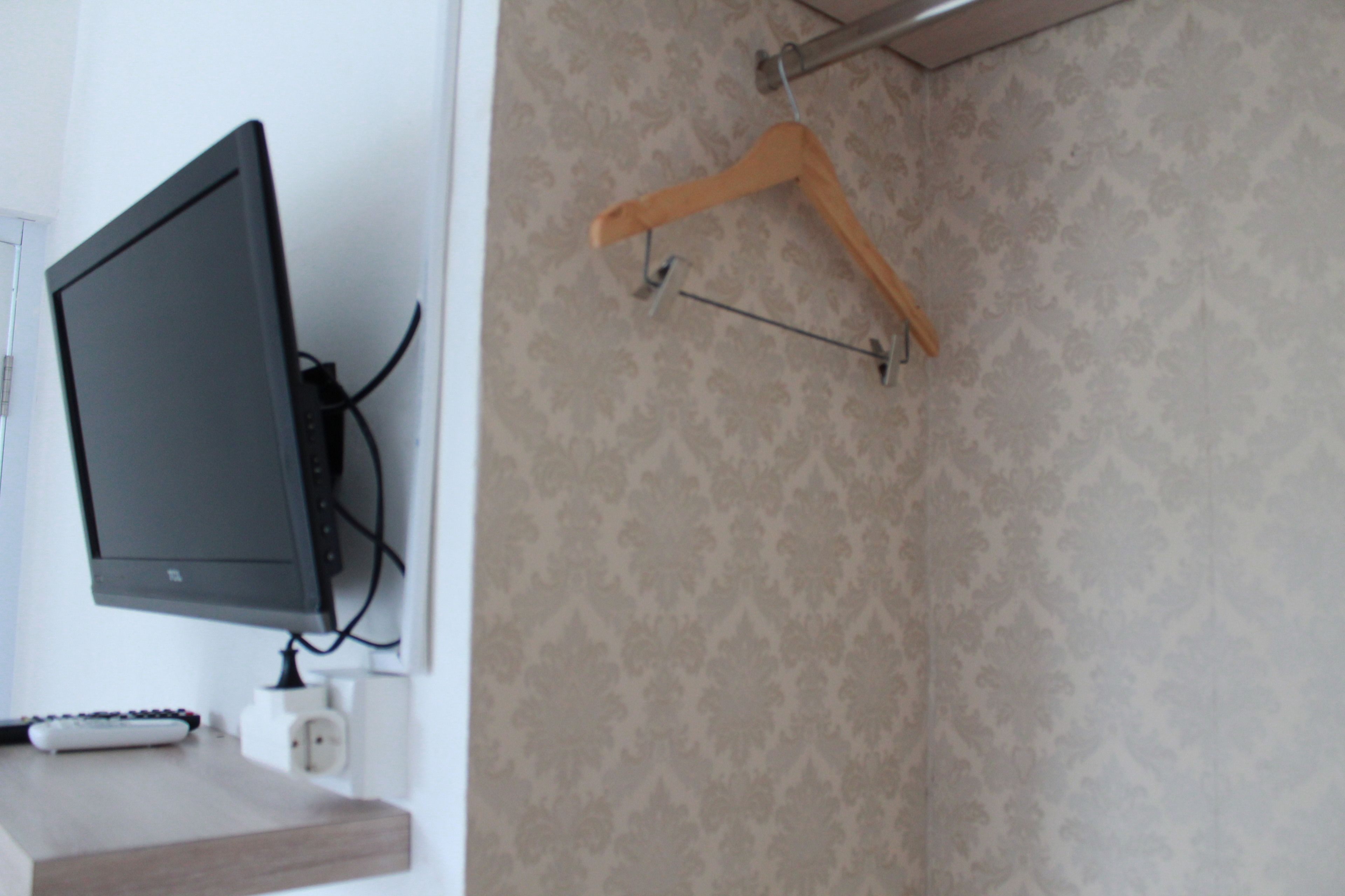 Habitación con televisión de pantalla plana montada en la pared, un perchero de madera y un enchufe en la pared.