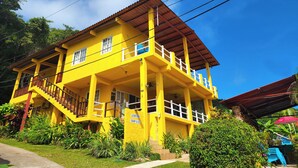 Un bâtiment jaune doté d’un balcon et d’un escalier, entouré de verdure.