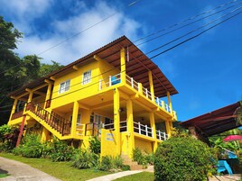 Un edificio amarillo con balcón y escaleras, rodeado de vegetación.