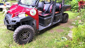 Un véhicule utilitaire rouge et noir est garé dans un jardin, entouré de pelouse et de plantes.