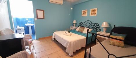 A bedroom with a bed, a desk, a chair, a ceiling fan, and a bathroom visible through an open door.