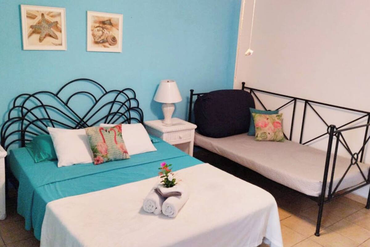 A bedroom with a bed, a daybed, a nightstand, a lamp, and two wall-mounted pictures.
