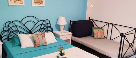 A bedroom with a bed, a daybed, a nightstand, a lamp, and two wall-mounted pictures.