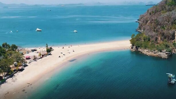Une plage aux eaux cristallines, avec des bateaux et un paysage vallonné.