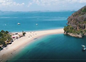 Una playa con aguas cristalinas, barcos y un paisaje montañoso.