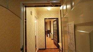 Un pasillo con suelo de madera, una puerta que da a otra habitación y una lámpara fijada en la pared.