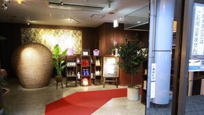 Un vestíbulo de hotel con alfombra roja, un jarrón grande con textura, repisas con artículos de tocador y una pared con diseño decorativo.