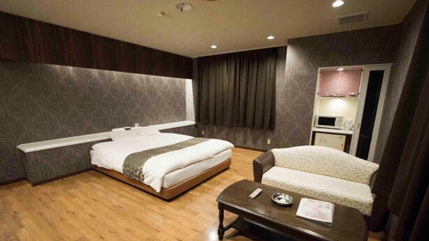 Habitación de hotel con una cama grande, un sofá, una mesita de centro y un microondas en una esquina.