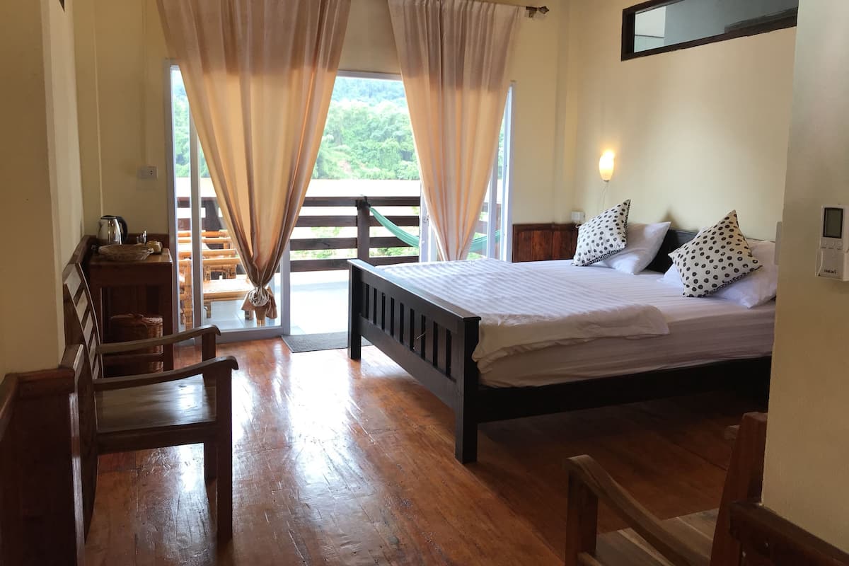 Un dormitorio con cama de madera, una mesita de noche y vistas al exterior a través de una ventana con cortinas.