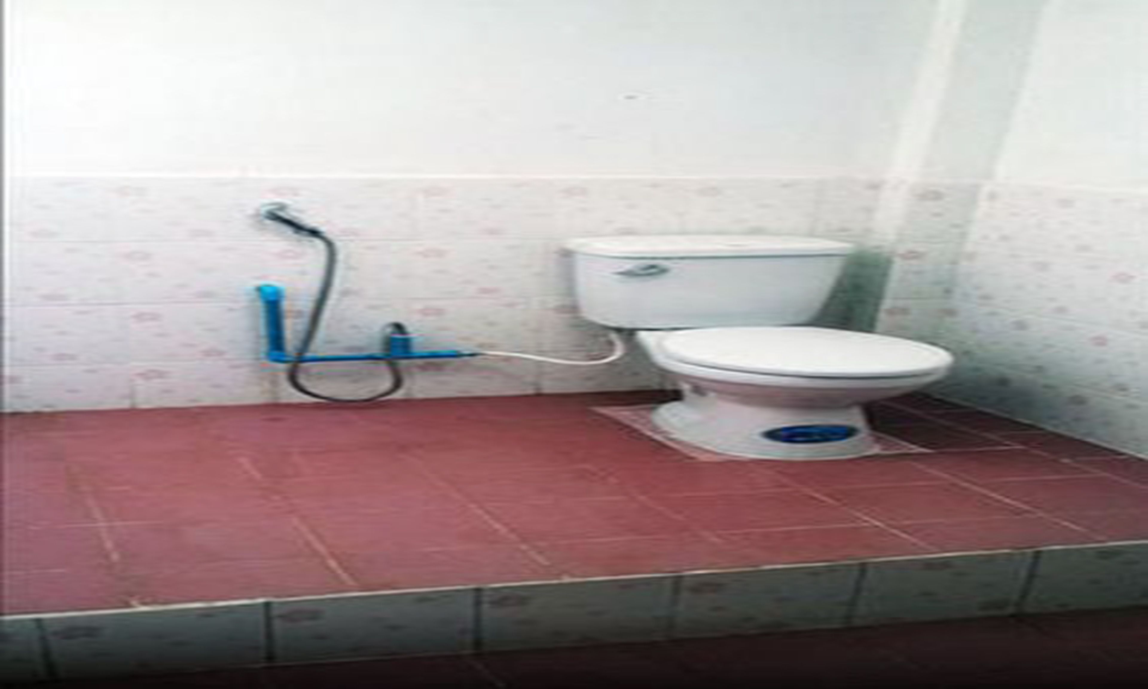 A small bathroom with a toilet, a blue pipe, and a red floor.