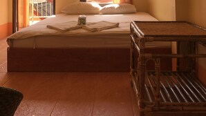 Een kamer met een bed, een tafel, een plafondventilator, een raam met gordijnen en uitzicht op een bergachtig landschap.