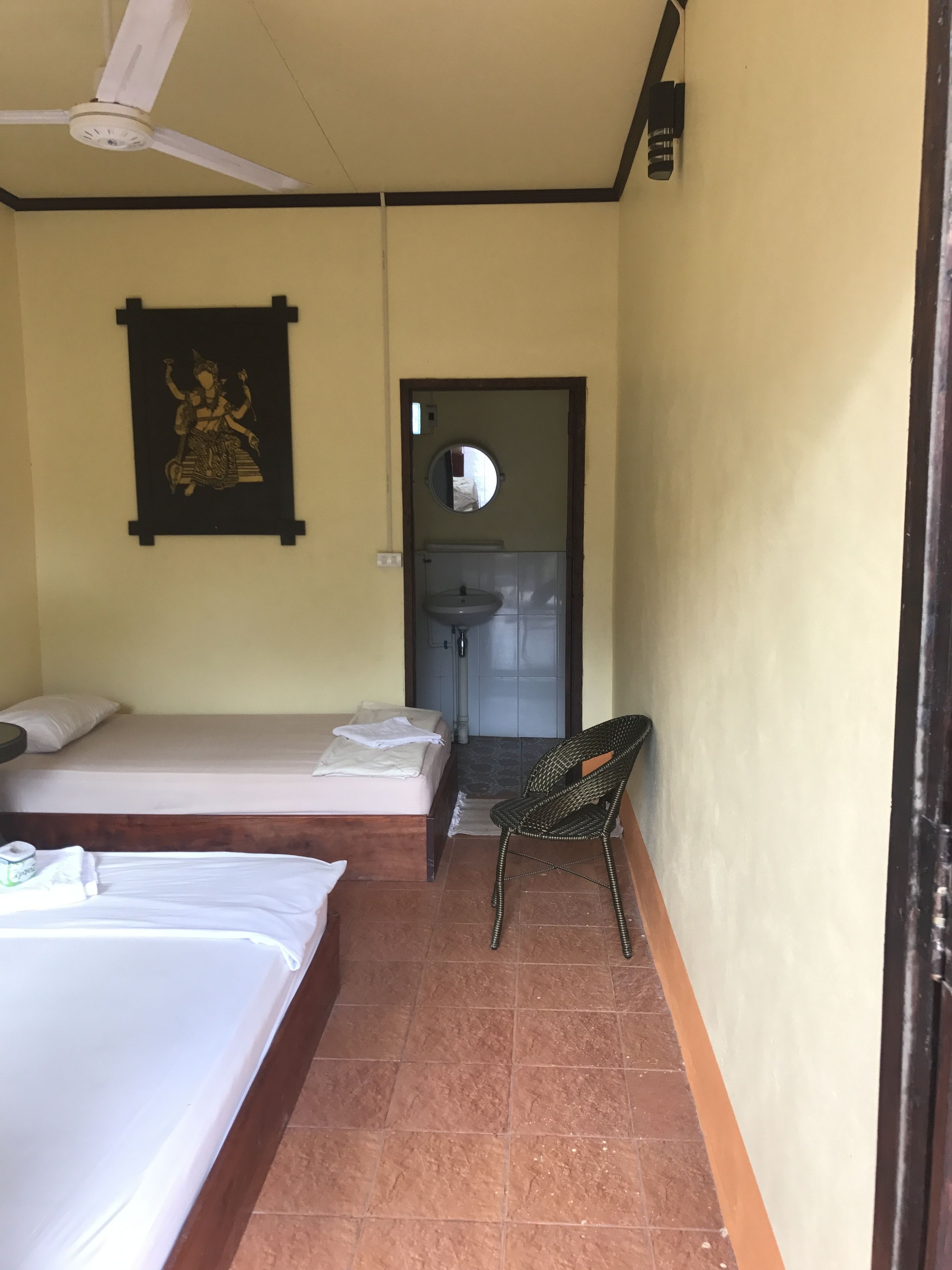 A room with two beds, a ceiling fan, a wall-mounted mirror, and a chair.
