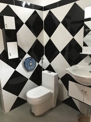 Bagno con parete a motivi a diamante in bianco e nero, un WC bianco, un portasciugamani blu, un lavandino bianco con uno specchio sopra e un armadietto bianco sotto il lavandino.