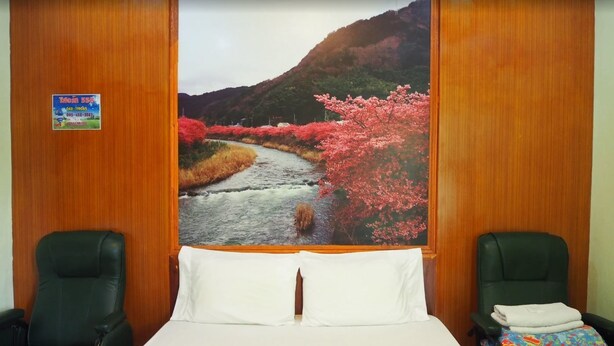Habitación de hotel con una cama, dos sillas, una pared de madera y un cuadro grande de un río y flores de cerezo.