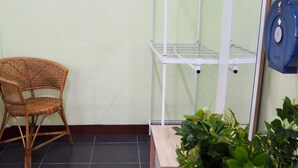 Una habitación con una silla de mimbre, un estante blanco y una planta en maceta.