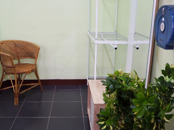 Una habitación con una silla de mimbre, un estante blanco y una planta en maceta.