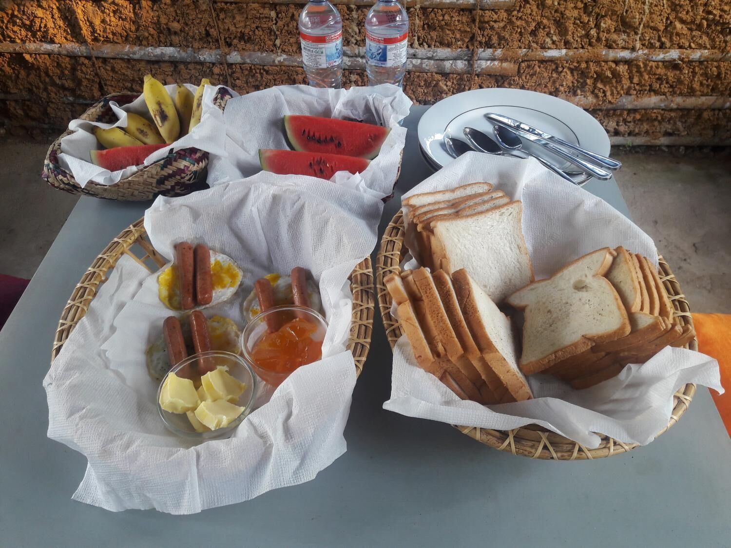 A table with baskets containing sliced bread, hot dogs, eggs, and condiments.